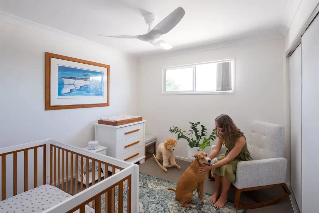 Mulher sentada em uma cadeira brincando com um cachorro Golden dentro de um quarto com ventilador de teto ligado, destacando os benefícios do ventilador para conforto e bem-estar.