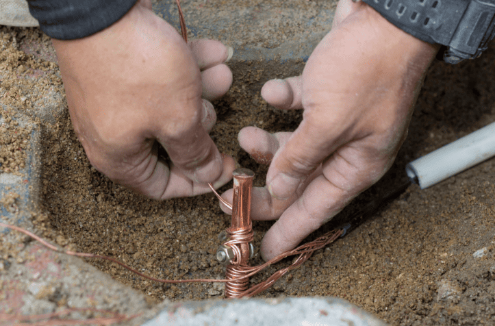 Mão instalando haste de aterramento no solo para sistema elétrico
