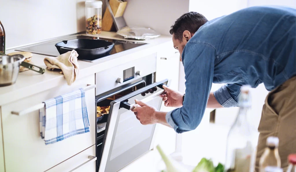Homem se curvando para abrir o forno de um fogão elétrico