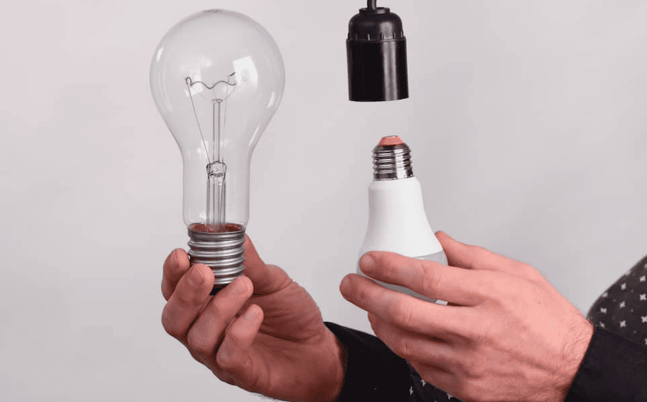 Homem segurando duas lâmpadas, uma incandescente e uma LED, comparando eficiência energética
