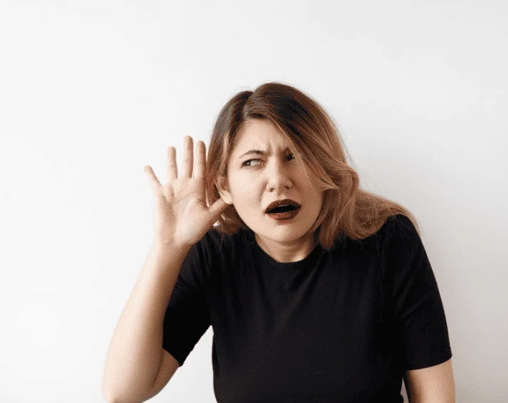 Mulher com a mão no ouvido tentando ouvir som vindo da parede