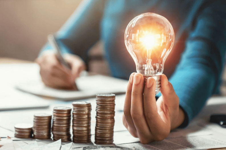 Homem segurando lâmpada incandescente enquanto faz contas, simbolizando economia de energia