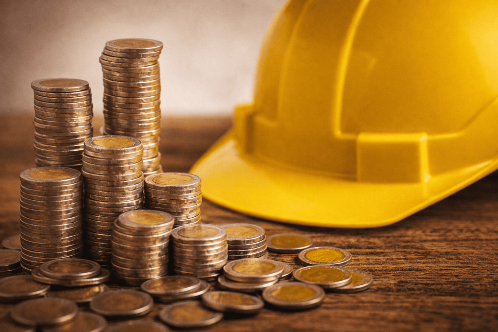 Capacete amarelo de segurança sobre mesa com moedas de real