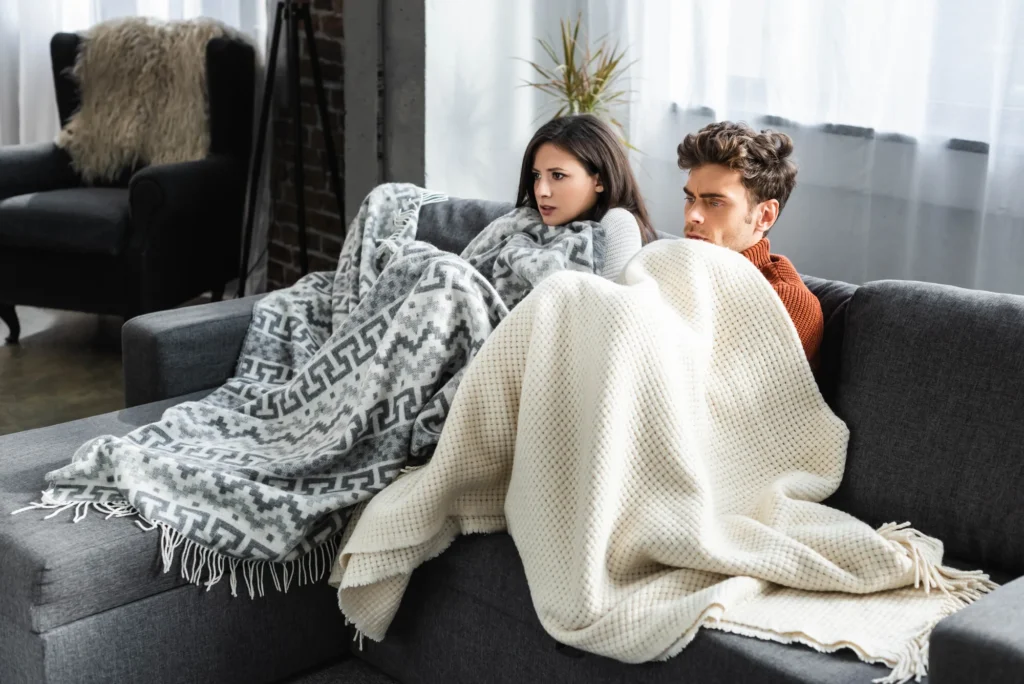 Casal com frio no sofá usando ar condicionado muito gelado