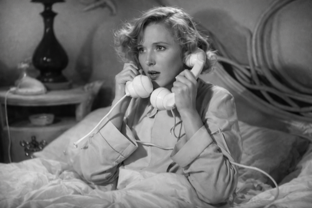 Jean Arthur usando telefone clássico em cena de filme antigo